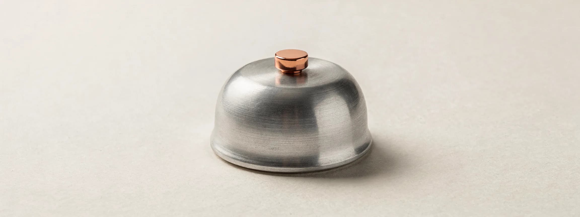 A brushed steel table bell with a polished copper button, on paper.