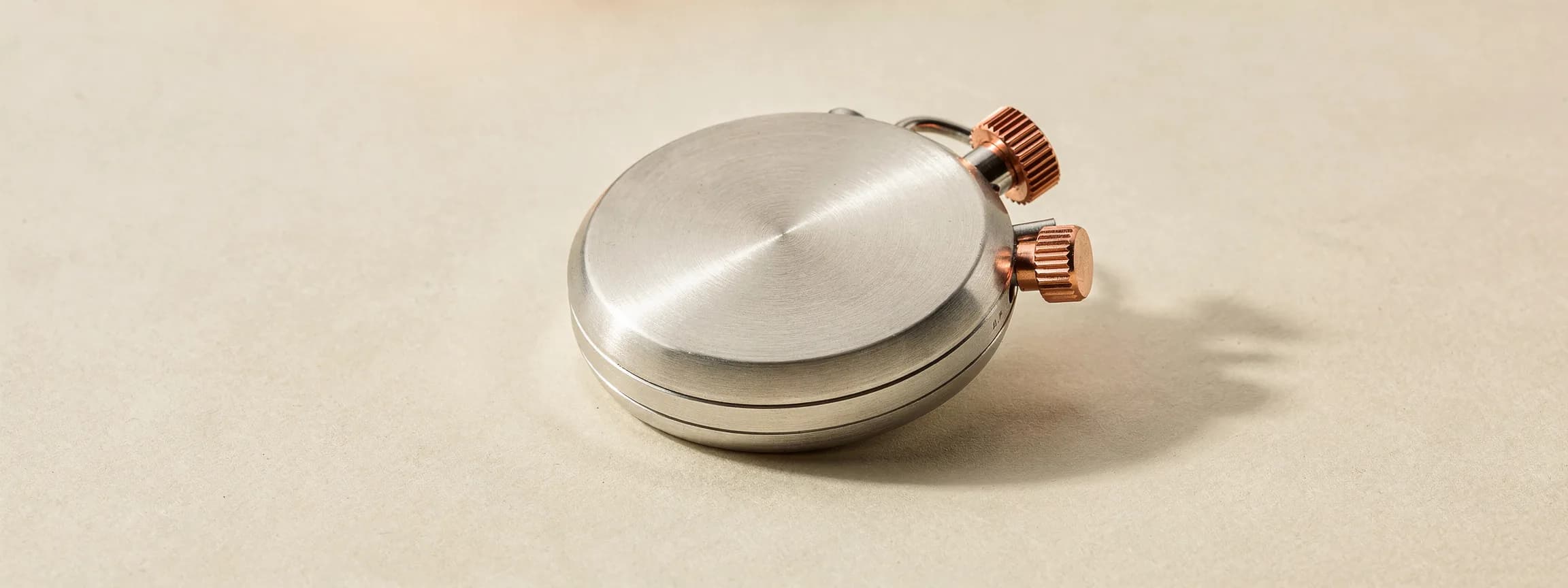 A brushed steel stopwatch with a copper crown, on paper.
